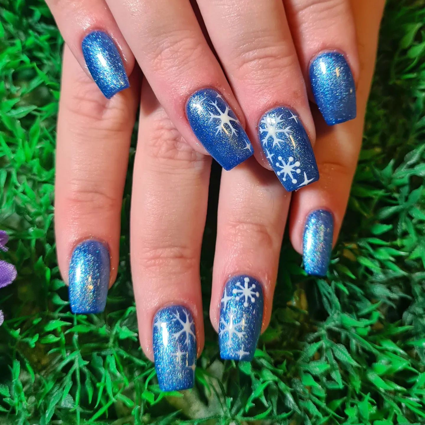 Blue glittered nails look like the sky and snowflakes fall from the sky in this image. The nail art and nail polish go with each other.