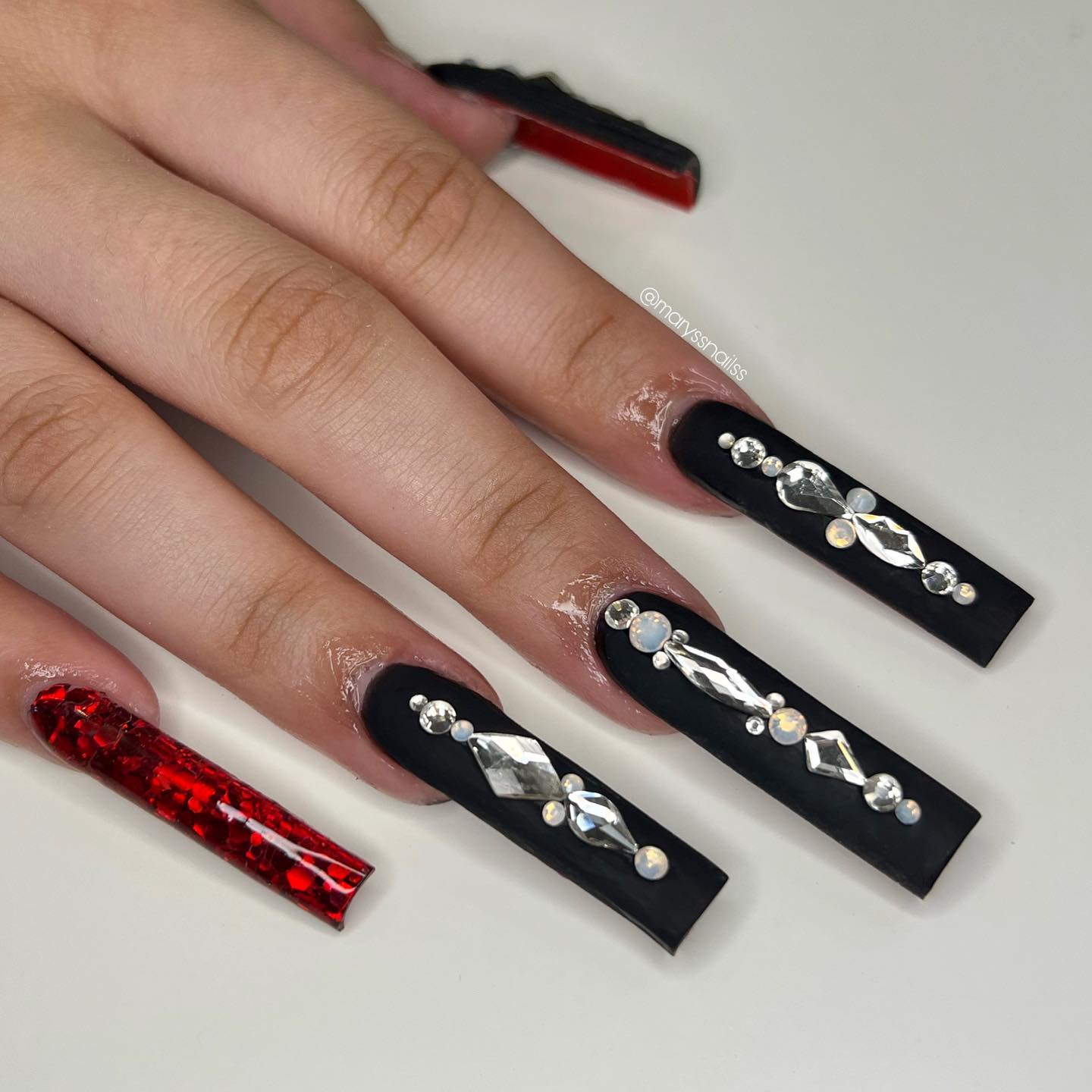 Long acrylic nails are super cool and you have to be bold to get it, right? To add these nails an extra beauty and boldness, let's apply a black matte nail polish with stones on them and a shiny red nail polish.